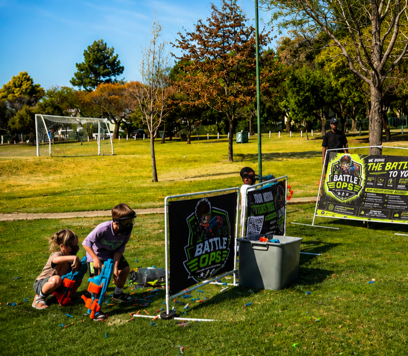 Battle Ops battle barriers, branded banners and dart bin set up outdoors for a kids Nerf party